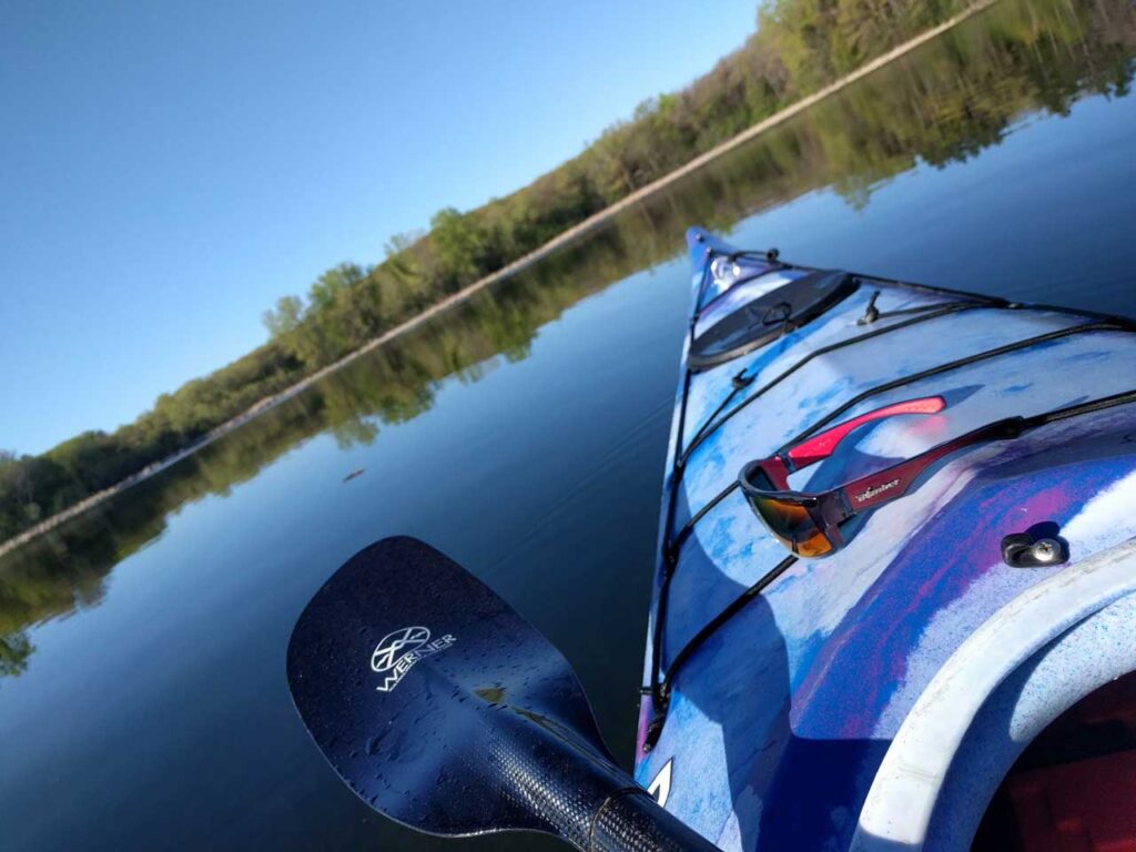 Descubre la Vida Bomber 30 Vista panorámica con vistas a un lago mientras está sentado en un kayak con gafas de sol Bomber